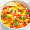 Closeup of a bowl of mango, avocado, red pepper, red onion salsa topped with a lime wedge and cilantro.