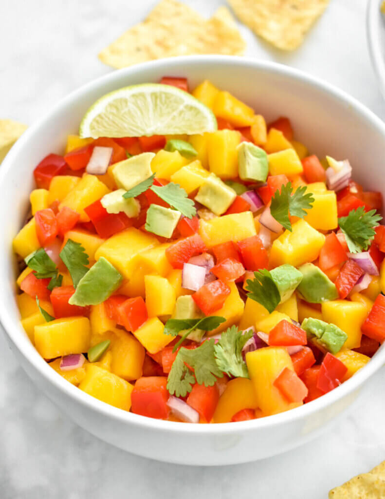 Closeup of a bowl of mango, avocado, red pepper, red onion salsa topped with a lime wedge and cilantro.