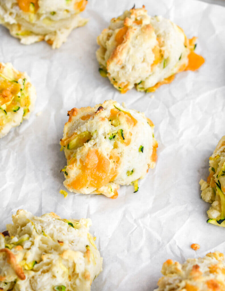 A parchment-lined tray of baked Zucchini & Cheese Biscuits.