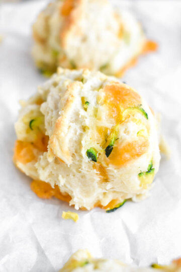 Close up of a Zucchini & Cheese Biscuits showing flecks of zucchini and cheddar cheese.