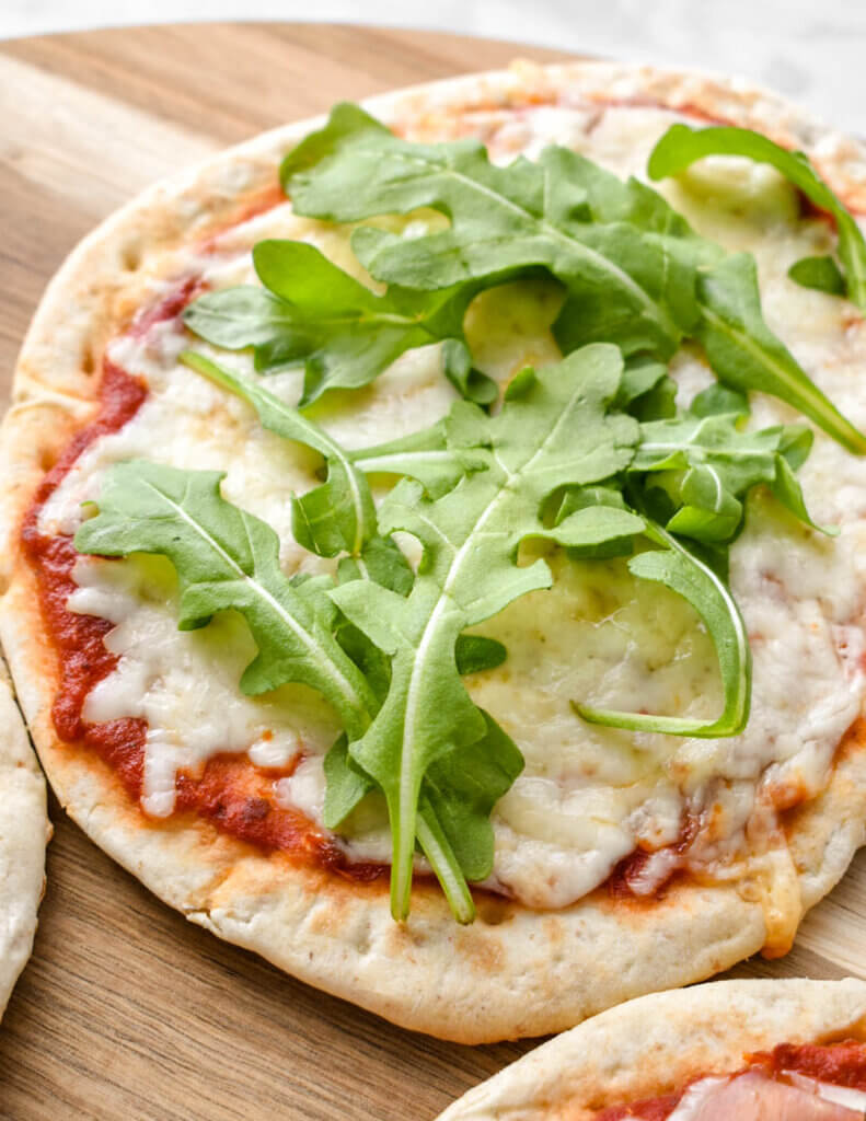 A simple cheese pita pizza topped with fresh arugula.