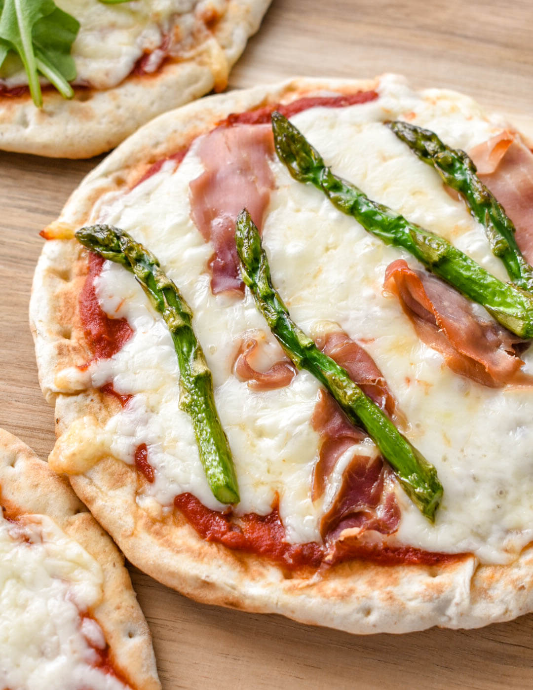 Closeup of a Pita pizza topped with prosciutto and asparagus.