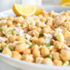 Closeup of chickpea salad with flakes of tuna, red onion, feta and fresh dill served with lemon wedges.