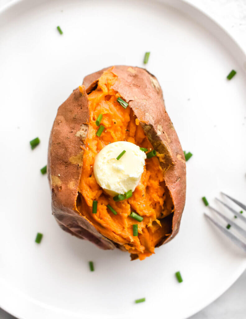 A baked sweet potato cut open and topped with butter and chives.