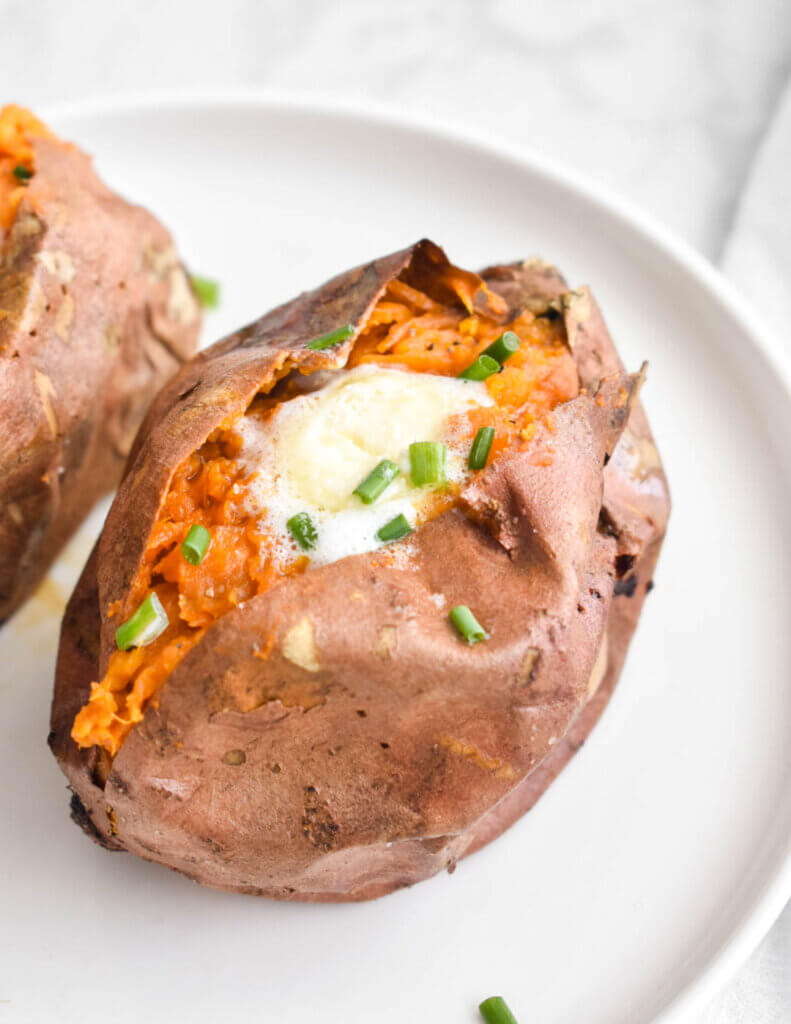 A closeup of a baked sweet potato with crispy skin that has been topped with butter and chives.