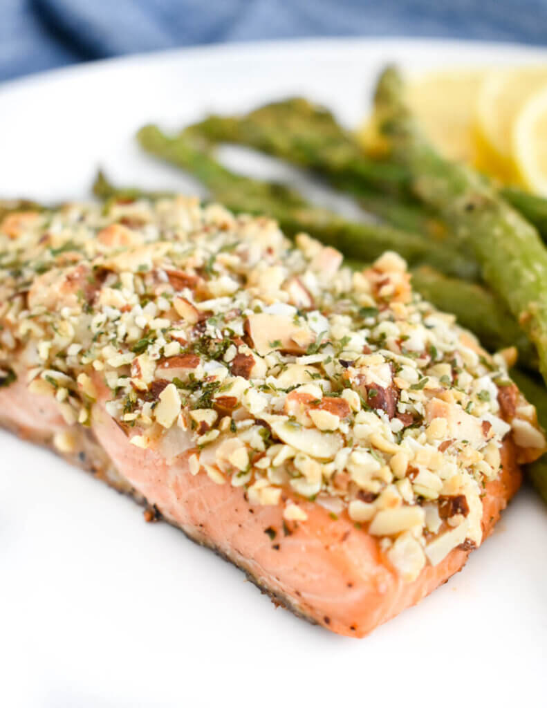 Almond crustes salmon on a white plate next to roasted asparagus spears.