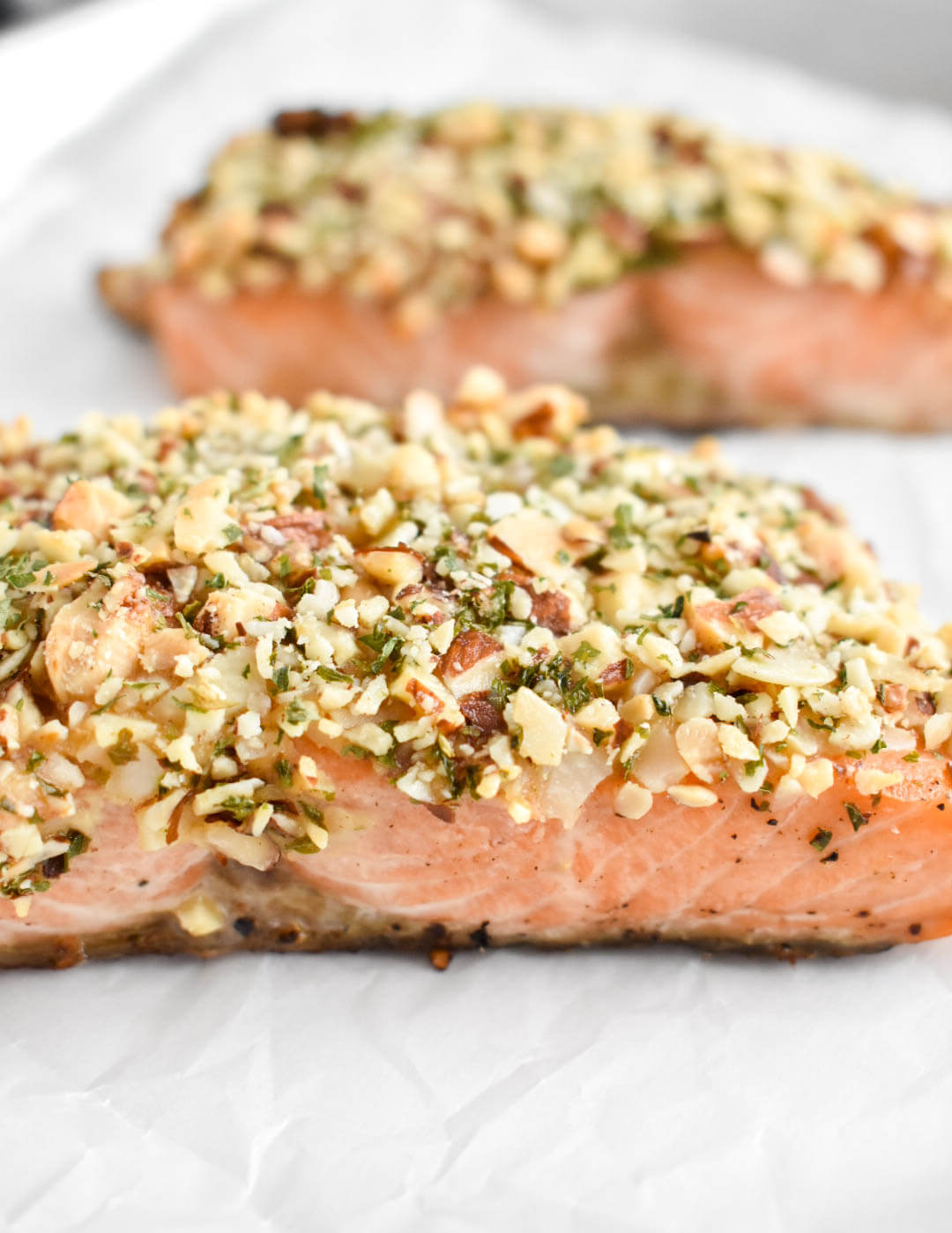 Closeup of two almond crustes salmon fillets on a baking sheet lined with parchment paper.