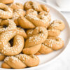 A plate of Greek Olive Oil Cookies- Koulourakia Ladiou topped with sesame seeds.
