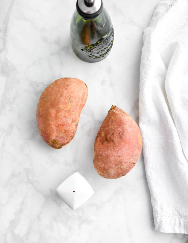 Ingredients for Air Fryer Baked Sweet Potatoes: Sweet potatoes, olive oil and salt on a marble counter top.