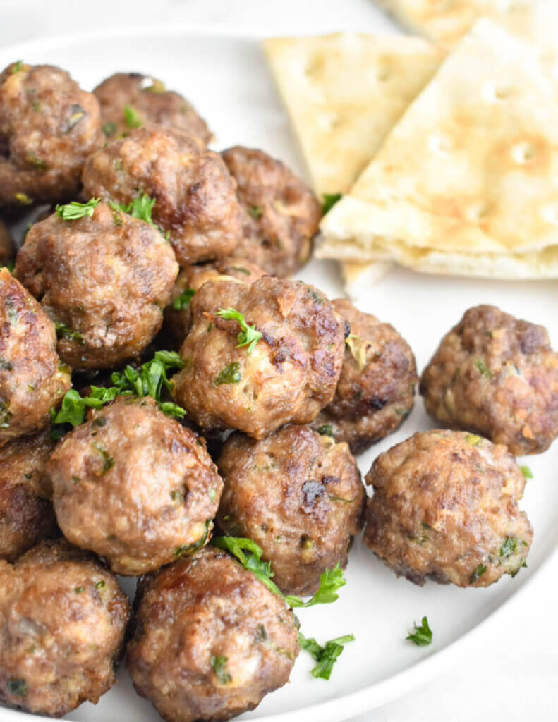 Closeup of a plate piled high with meatballs and sprinkled with parsley.