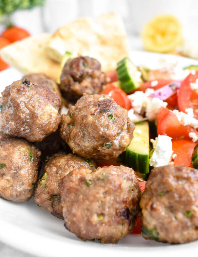 Closeup of meatballs in a bowl with Greek salad and a pita wedge.