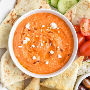 A bowl of tirokafteri dip sprinkled with feta and chili flakes on a mezze platter with pita and veggies.