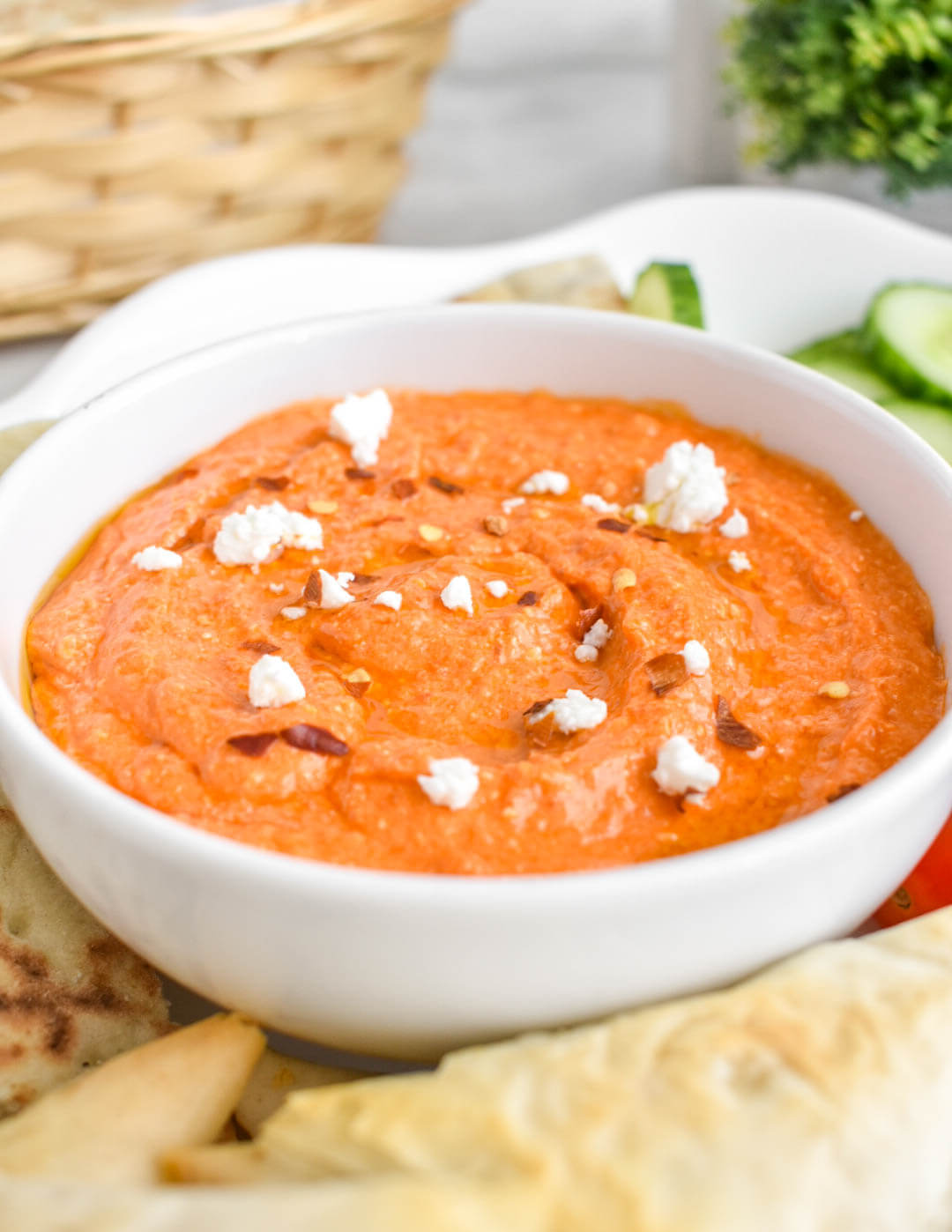 Closeup angled photo of a bowl of tirokafteri dip topped with chili pepper flakes and crumbled feta.