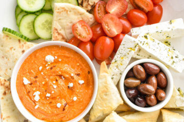 Closeup of a vegetarian mezze platter containing tirokafteri dip, spanakopitakia, cucumbers, tomatoes, olives and pita bread.