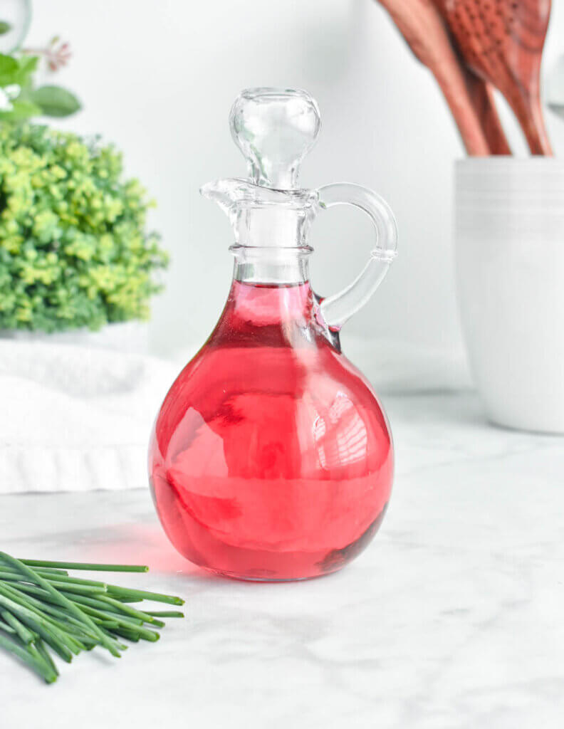 A bottle of pink chive blossom vinegar in a clear bottle.