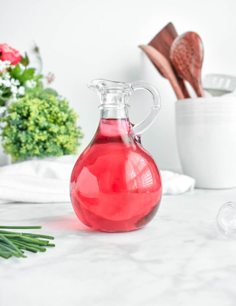 Pink chive blossom vinegar in a decorative glass bottle set on a marble counter top.
