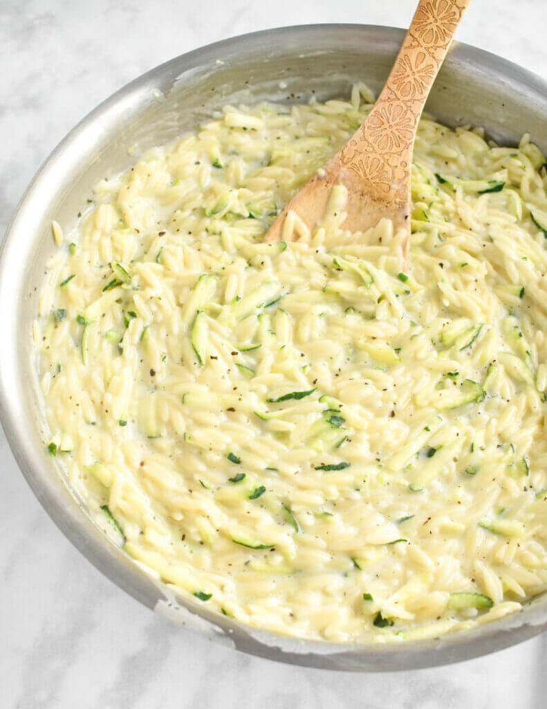 Closeup of a skillet of orzo and zucchini in a cream sauce.