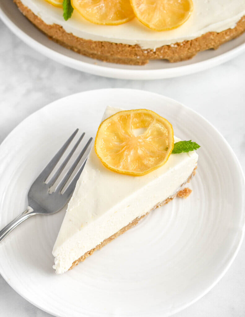 A slice of lemon cheesecake topped with a candied lemon slice on a white plate.