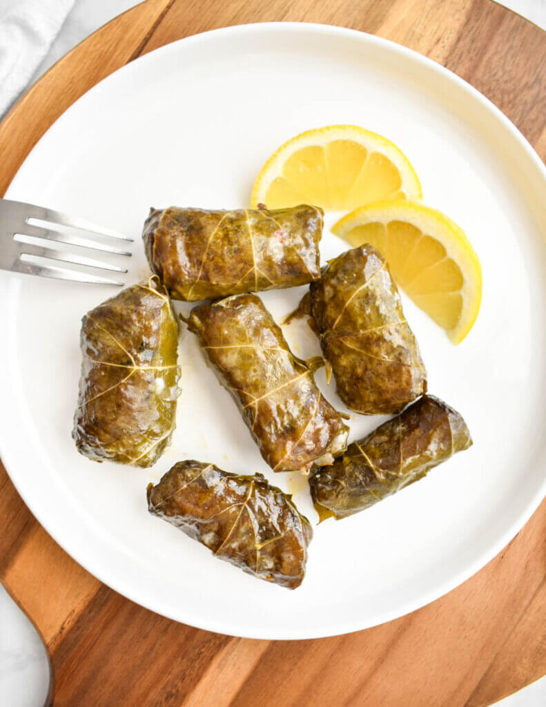 Dolmades on a white plate with lemon wedges.