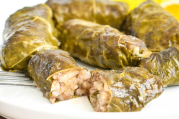 Dolmades on a plate with one sliced in half to show the rice and meat filling.