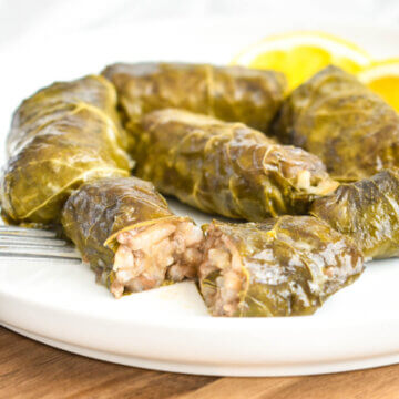 Dolmades on a plate with one sliced in half to show the rice and meat filling.