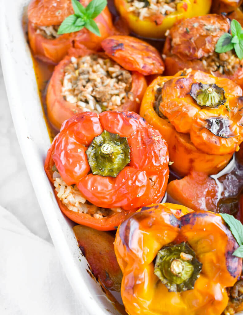 Closeup of baked stuffed pepeprs and tomatoes in a baking dish.