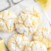 Lemon Crinkle Cookies piled on a small cooling rack surrounded by lemon wedges.