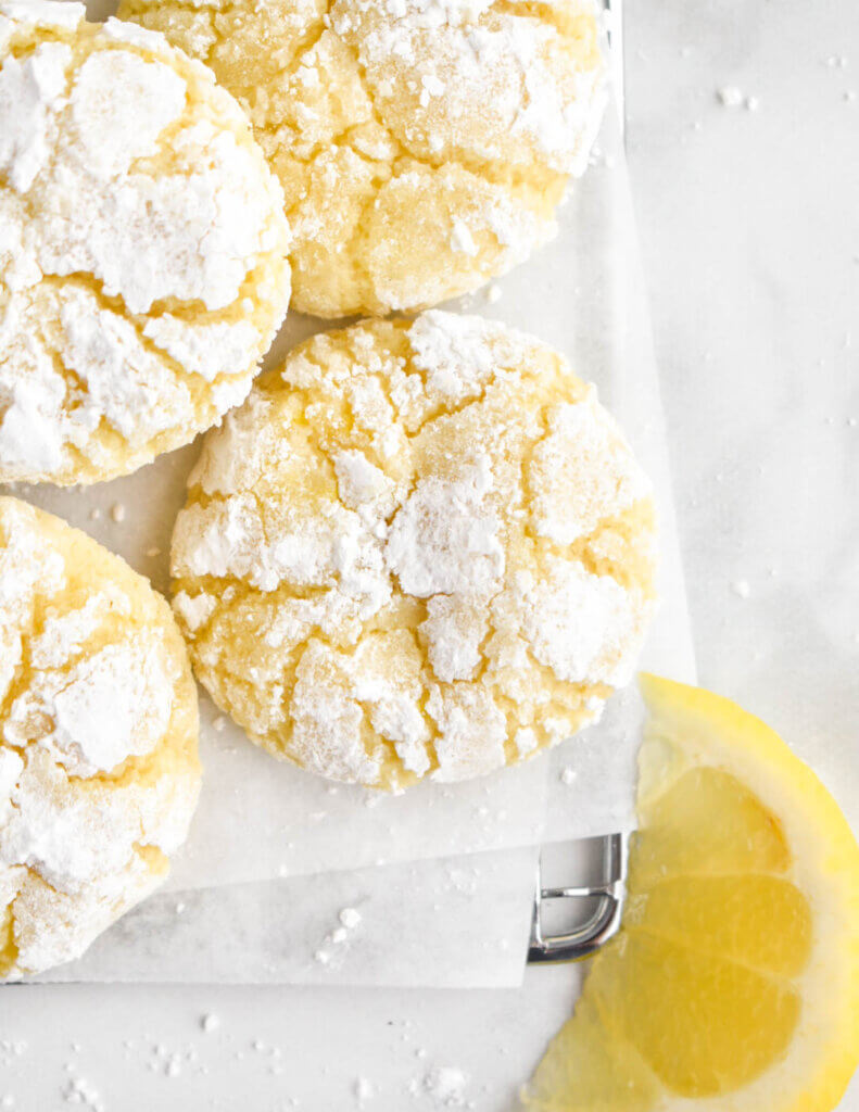 A lemon crinkle cookie close up set on parchment paper and with other cookies around it.