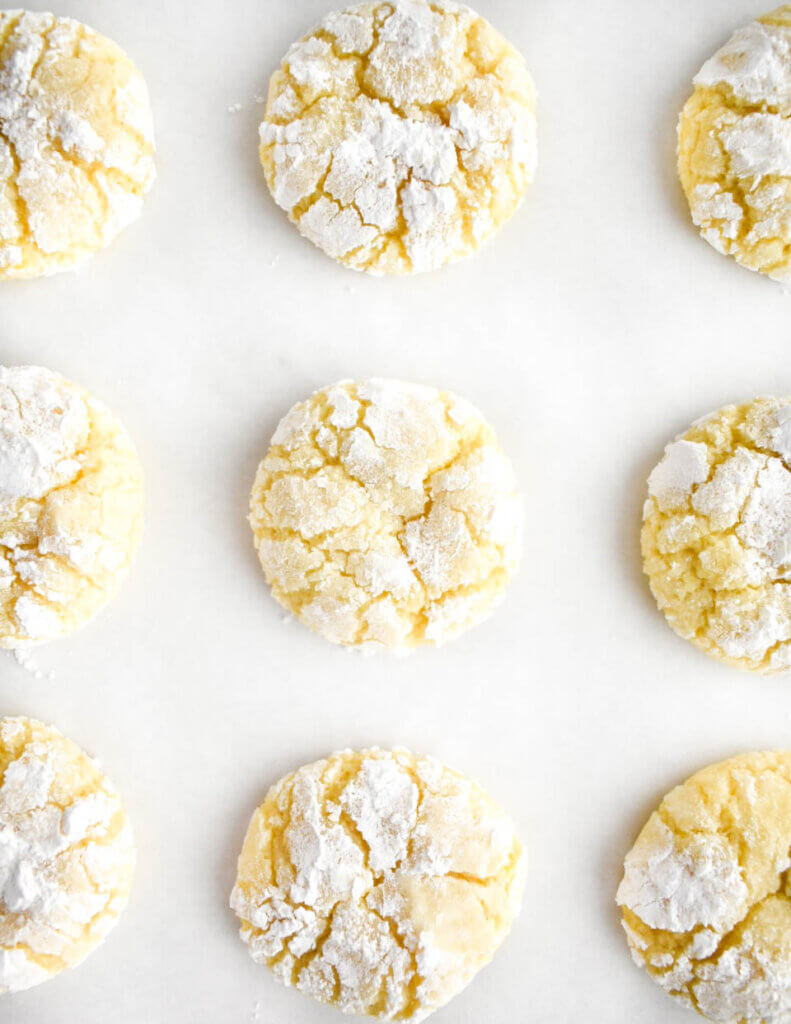 Lemon cookies dusted with powdered sugar on parchment paper.