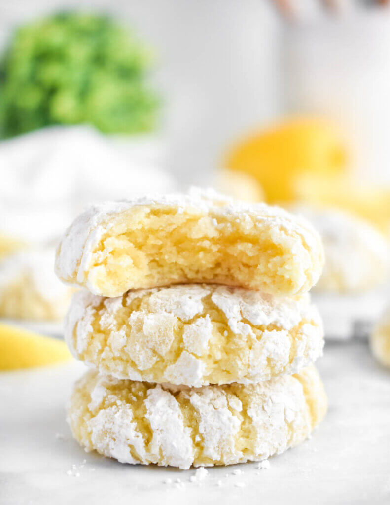 A stack of three lemon crinkle cookies with a bite taken out of the top one.