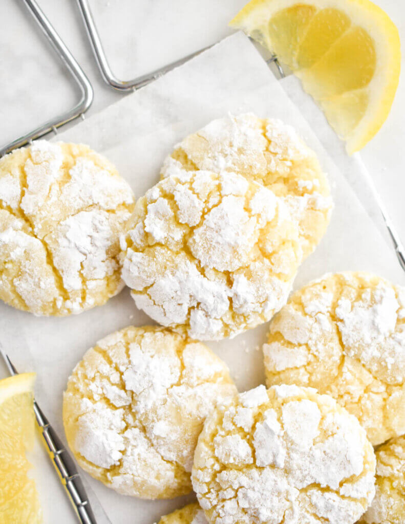 Lemon Crinkle Cookies piled on a small cooling rack surrounded by lemon wedges.