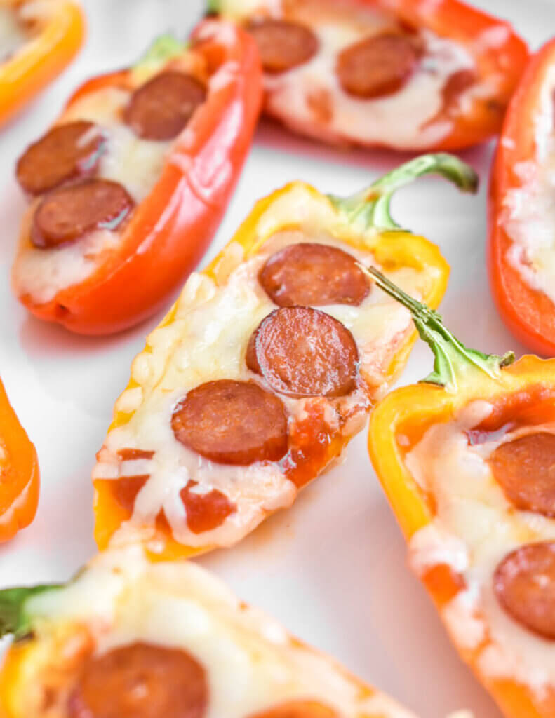 Closeup of pepperoni topped pizza mini peppers on a baking sheet.