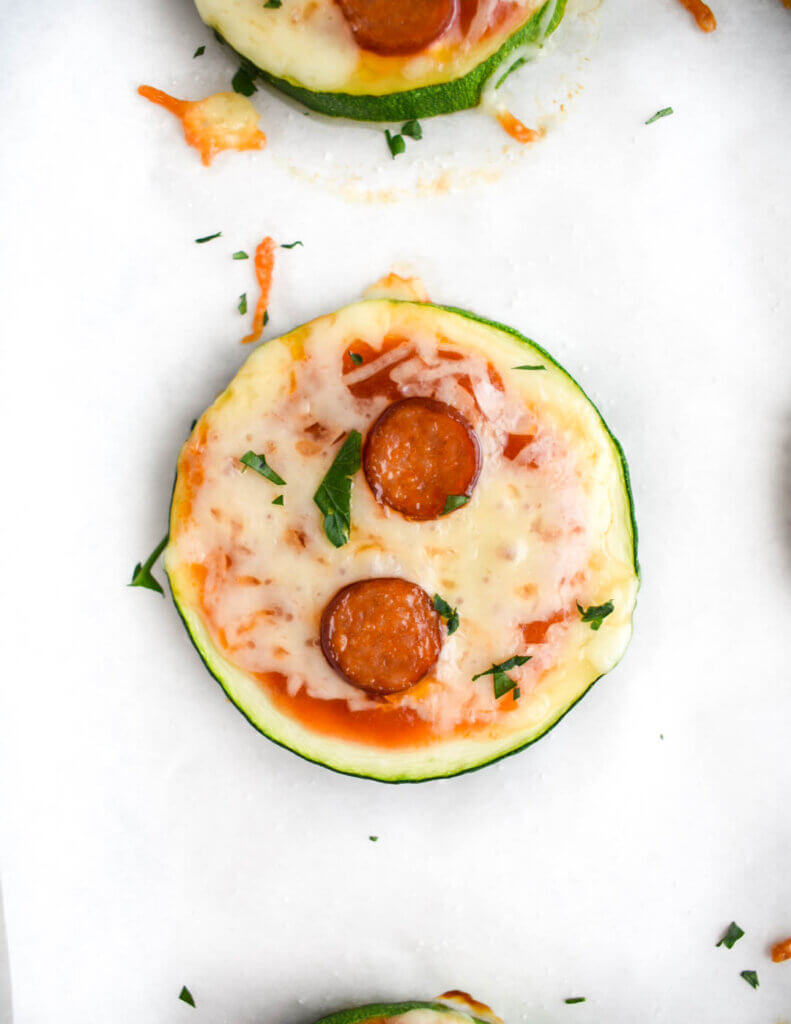 A zucchini pizza bite topped with mini pepperoni on a parchment lined tray.
