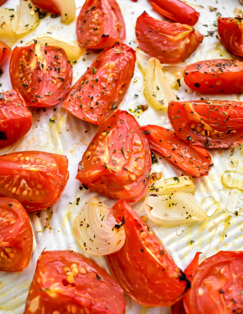 Roasted tomatoes, red pepper and onions on a parchment lined baking sheet.