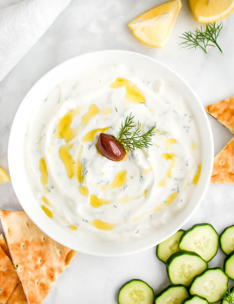 A bowl of tzatziki sauce served with pita wedges and sliced cucumber.