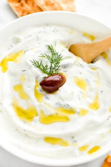 Tzatziki sauce drizzled with olive oil and topped with fresh dill and a kalamata olive.