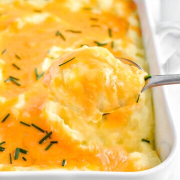 A scoop of cheesy baked mashed potatoes lifted out of the baking dish.