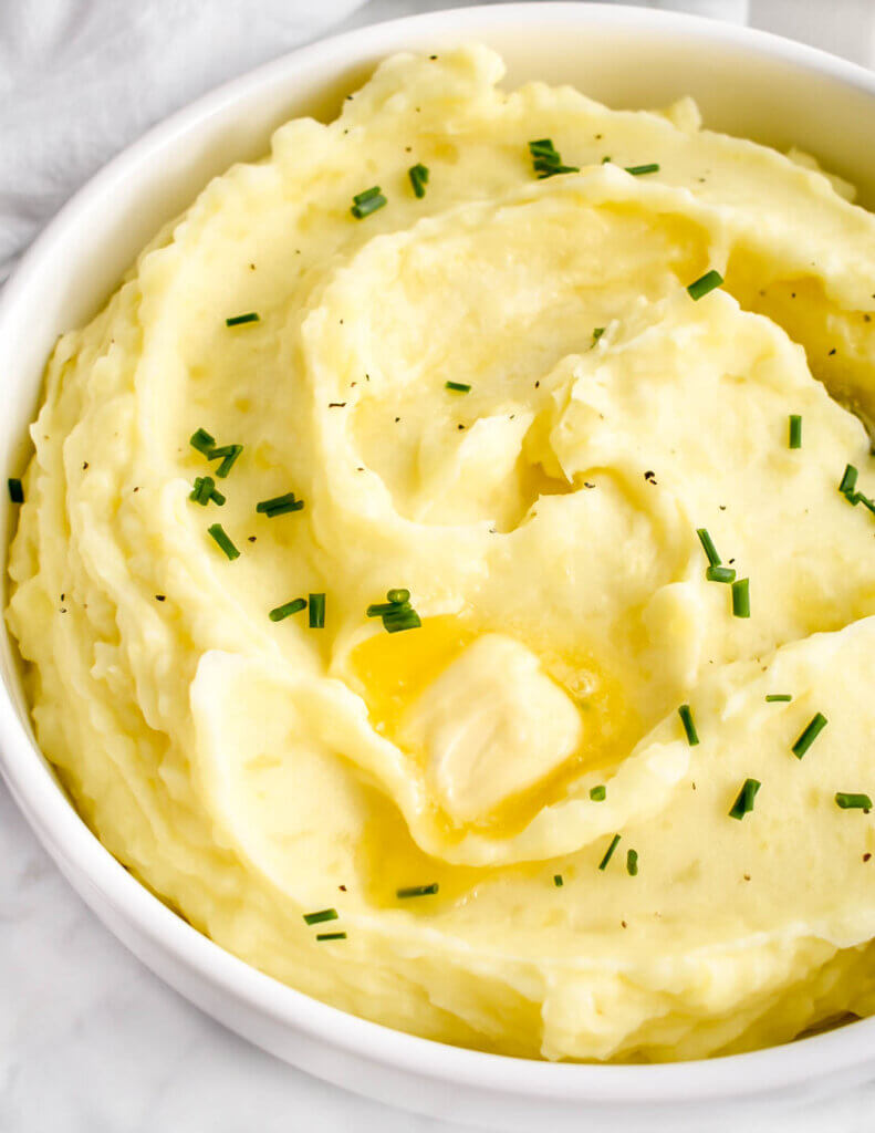 Close up of creamy whipped potatoes topped with chives and butter.