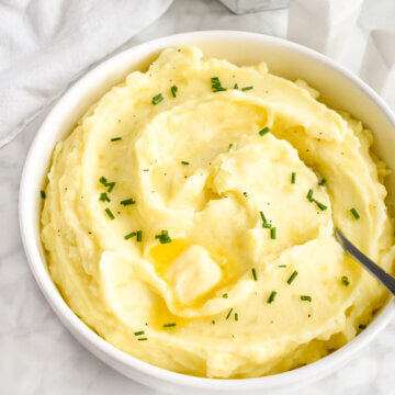 A bowl of creamy whipped potatoes topped with pats of butter and chives.