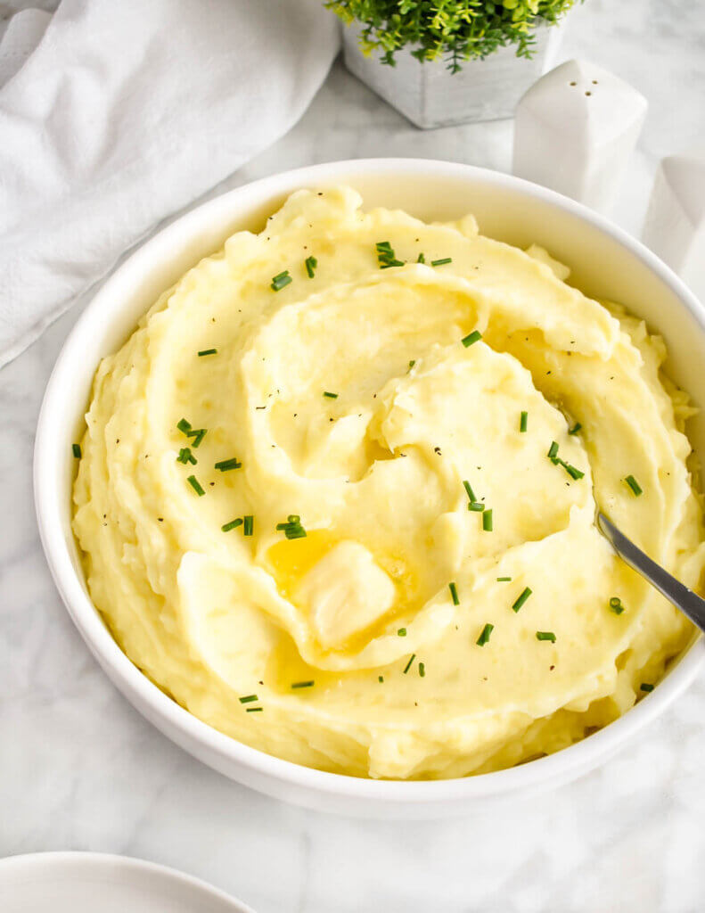 A bowl of creamy whipped potatoes topped with pats of butter and chives.