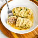 Greek cabbage rolls with avgolemono sauce in a white bowl.