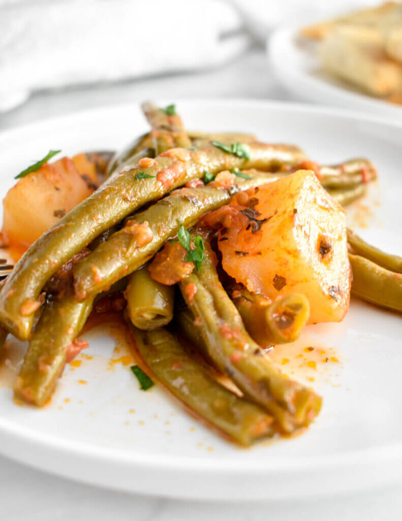 Close up of a plate of Greek green beans and potatoes in a tomato and herb sauce.