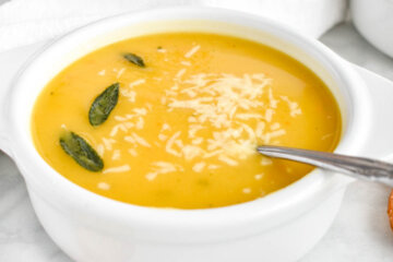 A bowl of acorn squash soup topped with parmesan cheese and crispy sage.