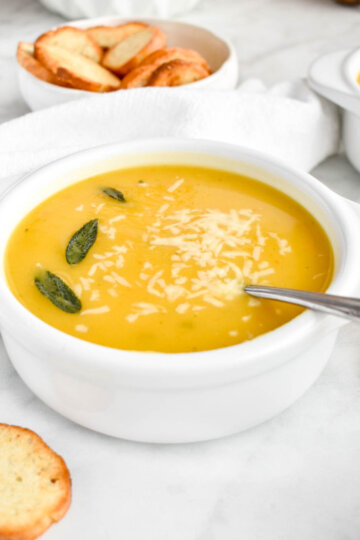A bowl of acorn squash soup topped with parmesan cheese and crispy sage.