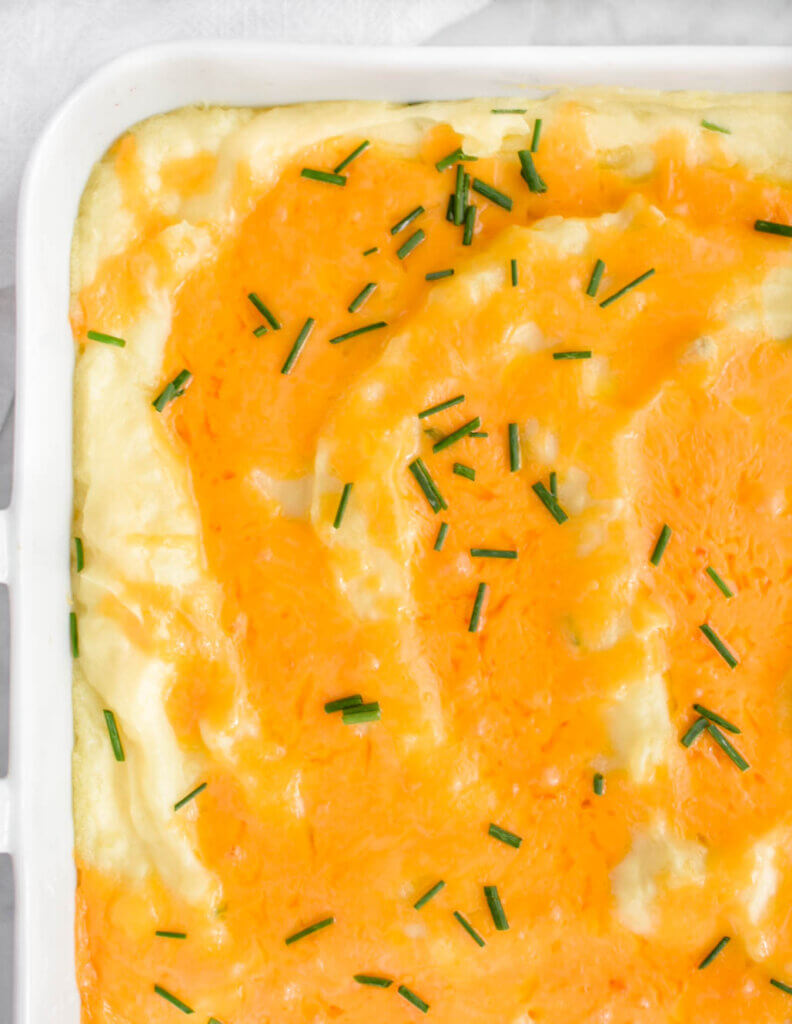 Closeup of baked mashed potatoes topped with melted cheddar and chives.