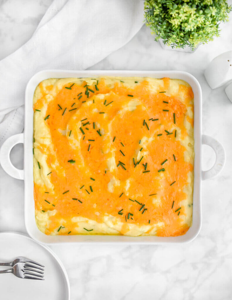 Cheesy baked mashed potatoes topped with melted cheddar in a square baking dish.