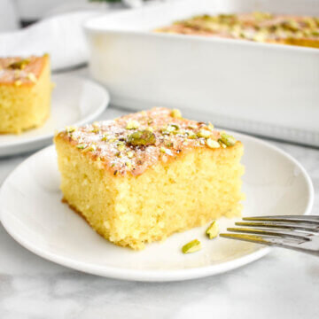A slice of ravani cake topped with powdered sugar and pistachios.