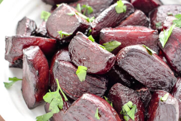 Roasted beets topped with fresh parsley in a white serving bowl.