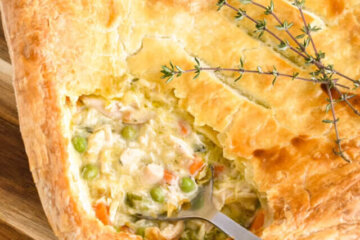 Closeup of a square turkey pot pie with the corner of pastry removed to show the creamy turkey filling being scooped up by a serving spoon.