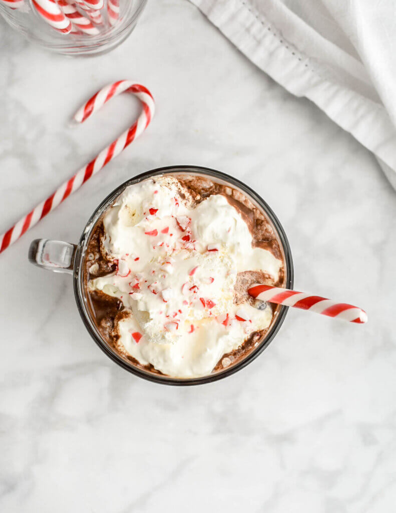 Topview of the whipped cream, crushed candy cane and candy cane stick garnishes on a mug of peppermint mocha set on a grey marble countertop.